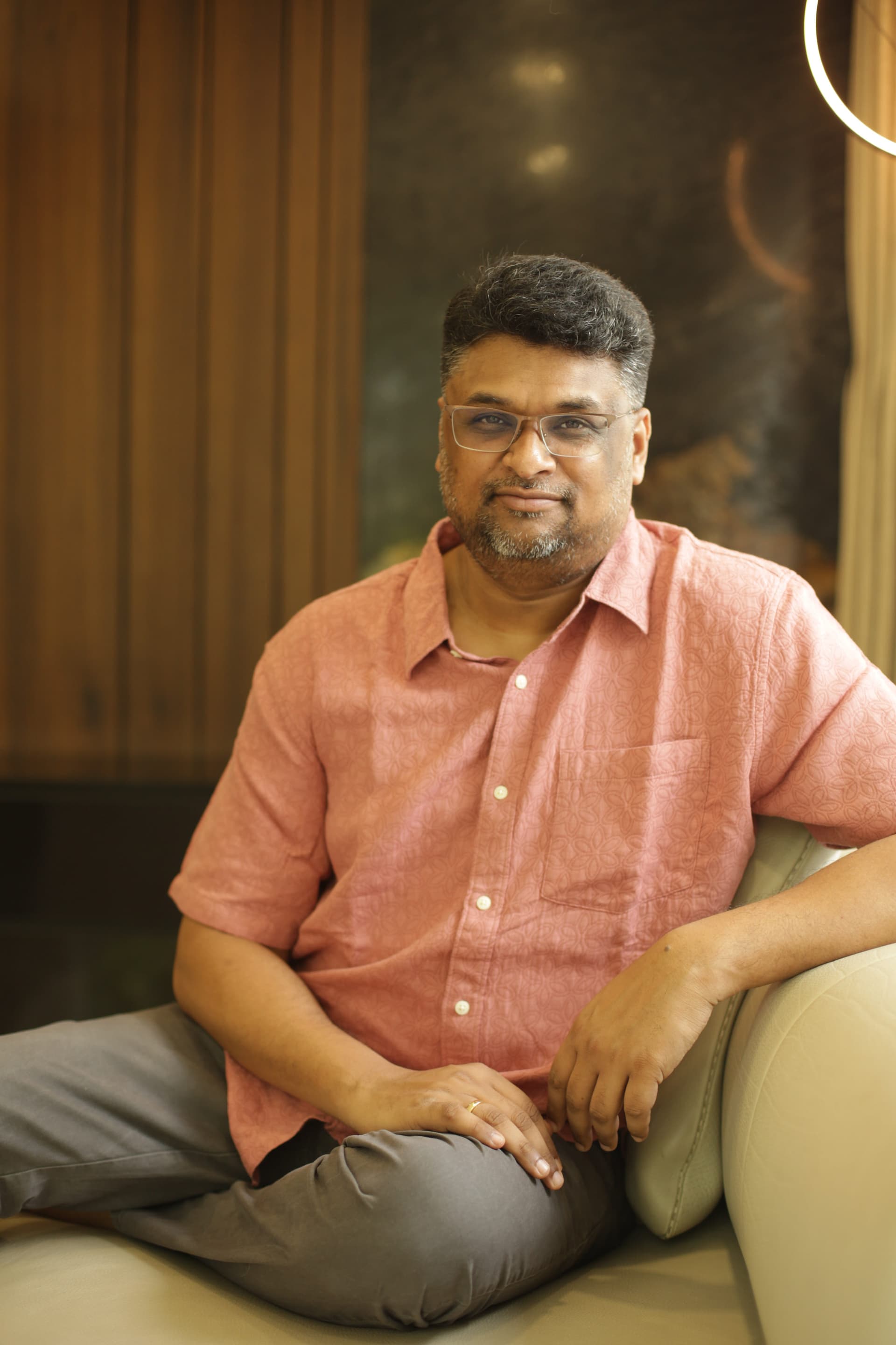 Hussain Sha Kiran seated in a coral shirt