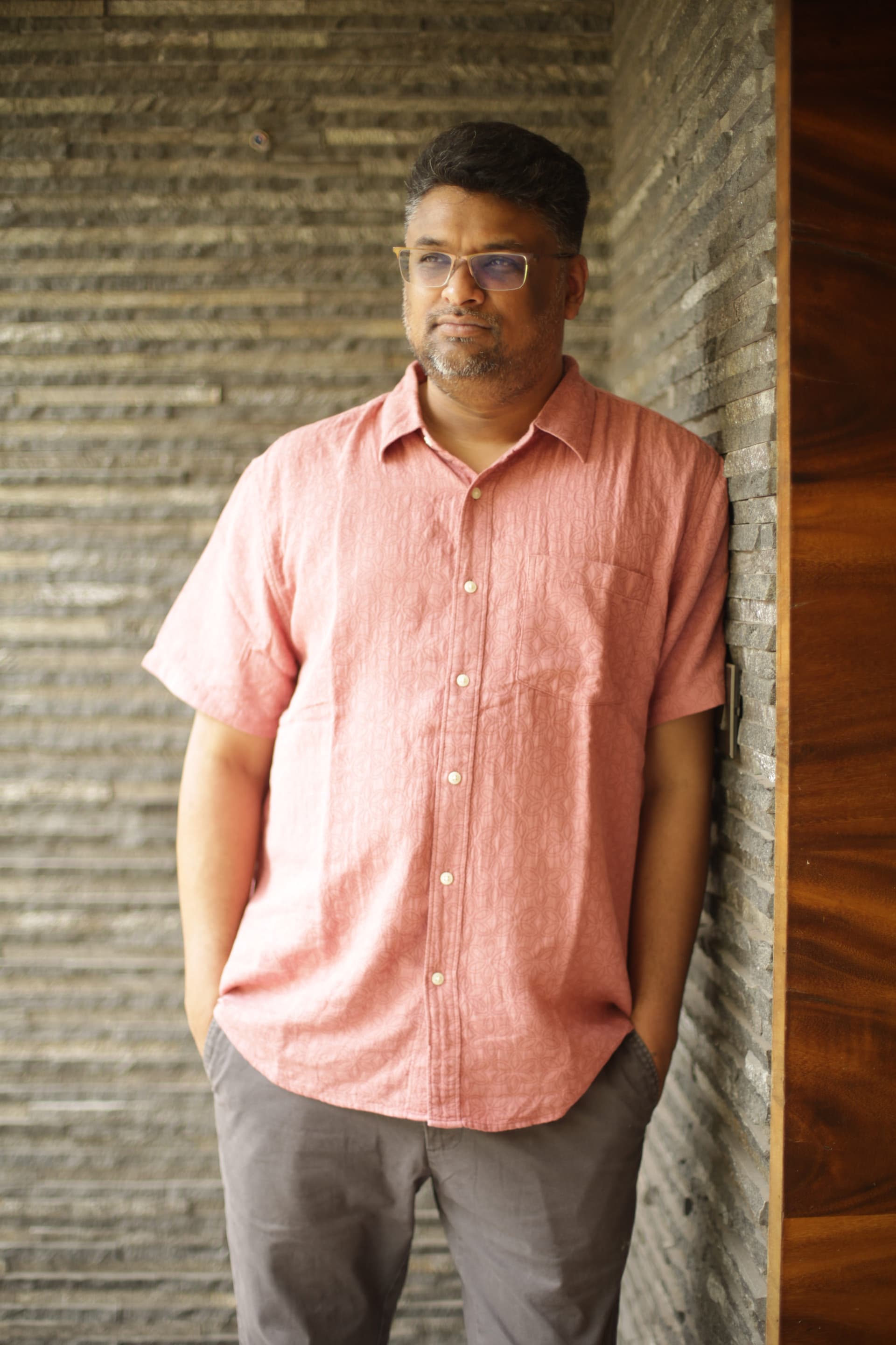 Hussain Sha Kiran standing beside a textured stone wall
