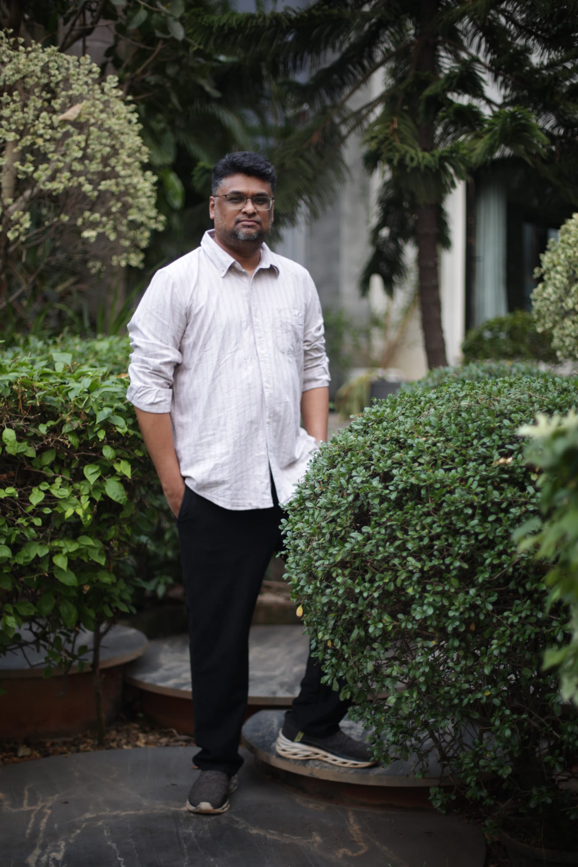 Hussain Sha Kiran standing in a garden in a white shirt